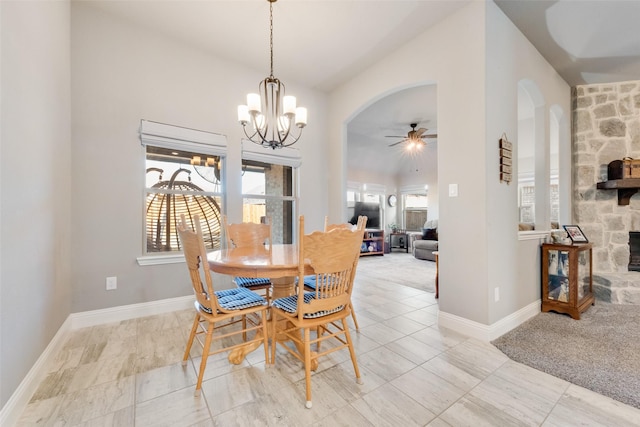 tiled dining area with vaulted ceiling, ceiling fan with notable chandelier, and a stone fireplace