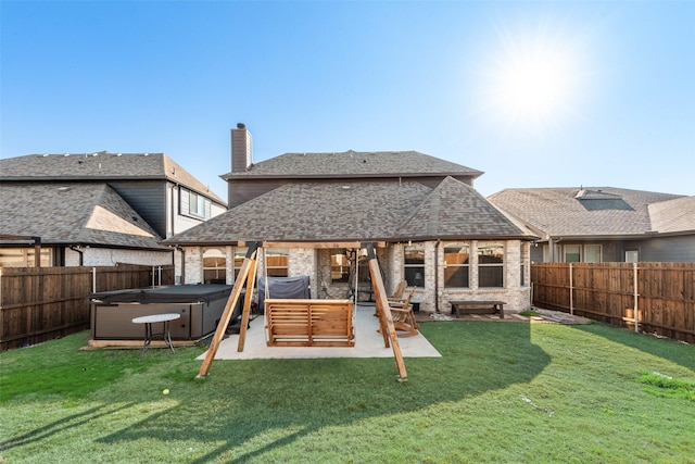 back of house featuring a hot tub, a lawn, and a patio