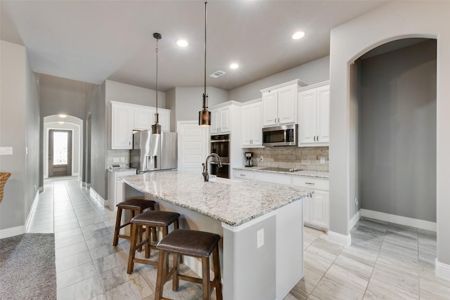 kitchen featuring stainless steel appliances, white cabinets, a center island with sink, and light stone countertops