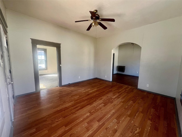 unfurnished room featuring arched walkways, heating unit, ceiling fan, and wood finished floors