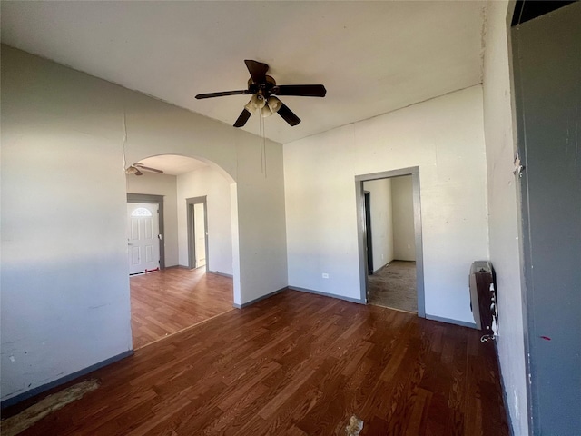 empty room with arched walkways, heating unit, ceiling fan, and wood finished floors