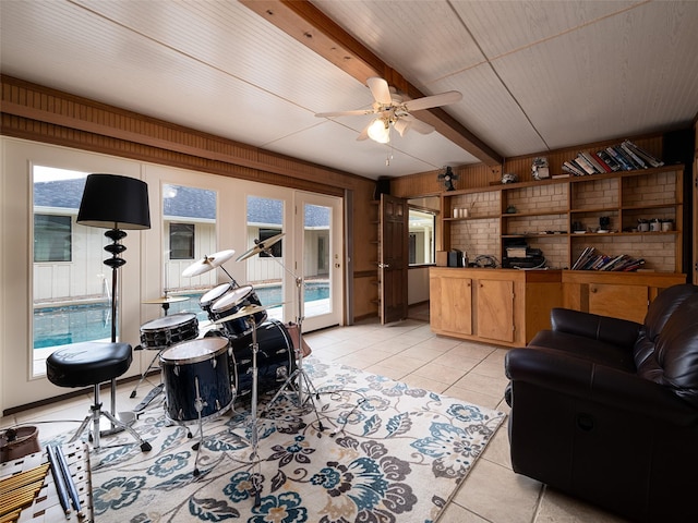 living room with wood walls, beamed ceiling, light tile patterned floors, and ceiling fan