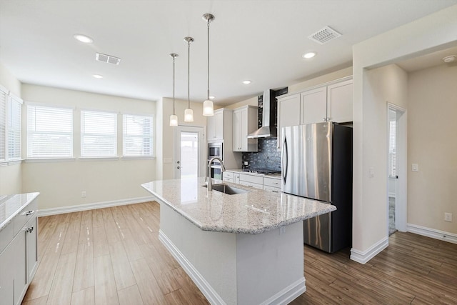 kitchen featuring stainless steel appliances, a kitchen island with sink, sink, wall chimney range hood, and white cabinets