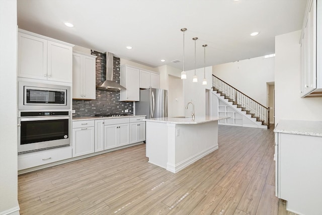 kitchen with white cabinets, appliances with stainless steel finishes, hanging light fixtures, and wall chimney range hood