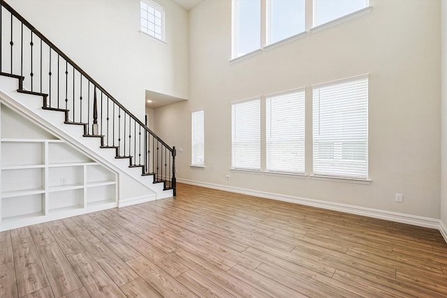 interior space with light wood-type flooring, built in shelves, and a towering ceiling