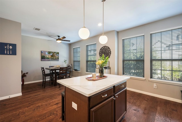 kitchen featuring dark brown cabinetry, a kitchen island, decorative light fixtures, dark hardwood / wood-style floors, and ceiling fan