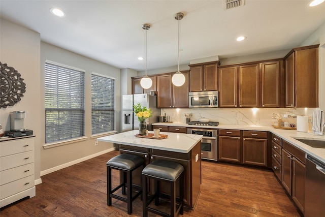 kitchen featuring appliances with stainless steel finishes, a center island, decorative light fixtures, dark hardwood / wood-style flooring, and tasteful backsplash