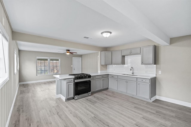 kitchen with sink, tasteful backsplash, stainless steel range with gas cooktop, kitchen peninsula, and gray cabinets