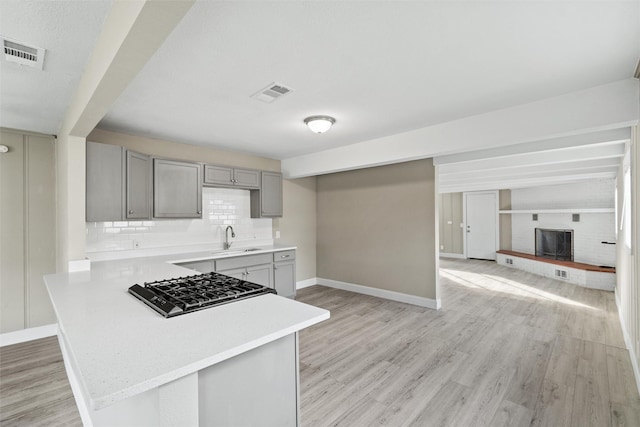 kitchen with gray cabinetry, stainless steel gas stovetop, sink, a fireplace, and light hardwood / wood-style floors