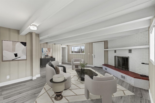 living room featuring beam ceiling, light wood-type flooring, and a brick fireplace