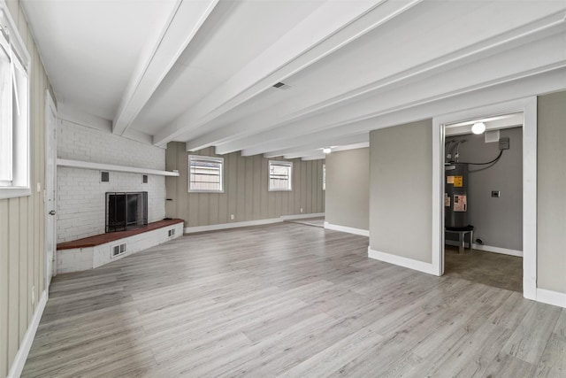 unfurnished living room with electric water heater, a fireplace, beamed ceiling, and light hardwood / wood-style floors