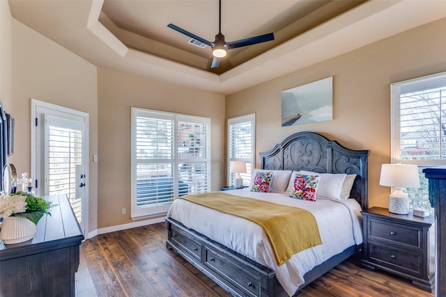 bedroom with dark hardwood / wood-style flooring, multiple windows, a raised ceiling, and ceiling fan