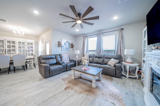 living room with a premium fireplace, ceiling fan with notable chandelier, and light wood-type flooring