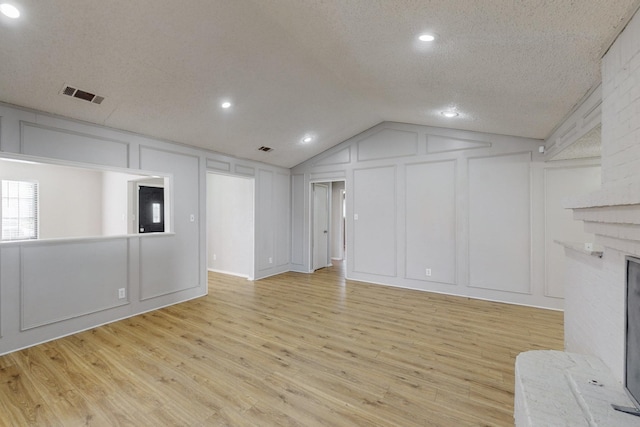 unfurnished living room featuring a fireplace, light wood-type flooring, a textured ceiling, and lofted ceiling