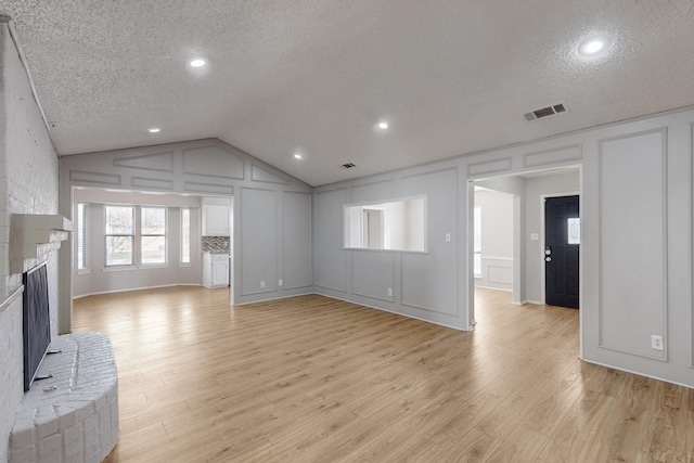 unfurnished living room with a textured ceiling, light hardwood / wood-style floors, lofted ceiling, and a fireplace