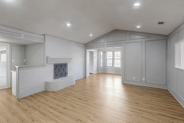 unfurnished living room featuring vaulted ceiling, a fireplace, light hardwood / wood-style floors, and a textured ceiling