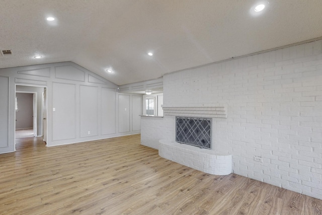 unfurnished living room with lofted ceiling, light wood-type flooring, a textured ceiling, a fireplace, and brick wall