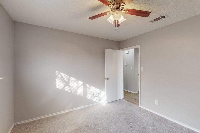 empty room featuring ceiling fan, light colored carpet, and a textured ceiling