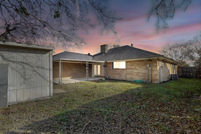 back house at dusk with a patio area, a yard, and central air condition unit