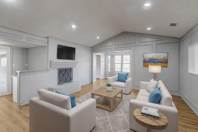 living room with a fireplace, light hardwood / wood-style floors, lofted ceiling, and a textured ceiling