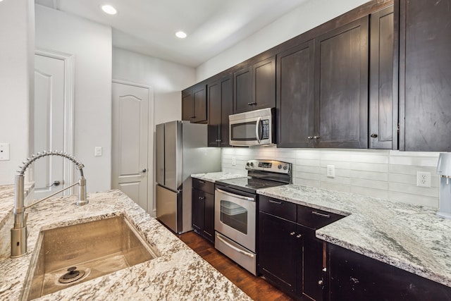 kitchen featuring dark wood-type flooring, sink, dark brown cabinets, light stone counters, and stainless steel appliances