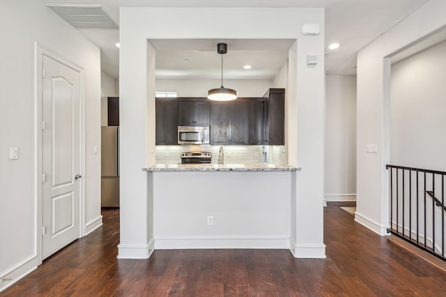 kitchen with hanging light fixtures, light stone counters, backsplash, dark brown cabinets, and appliances with stainless steel finishes