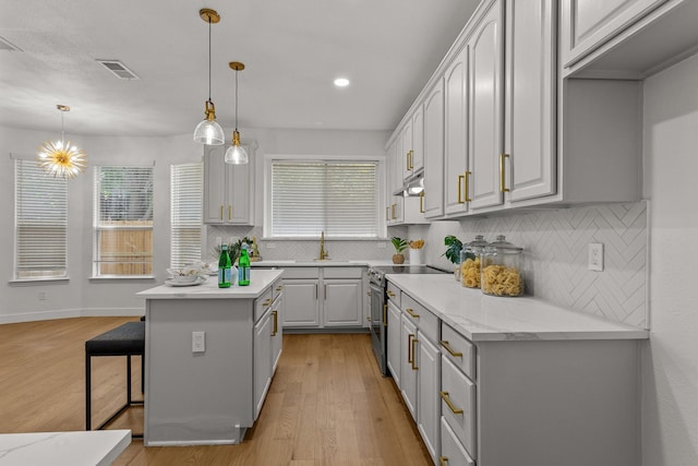 kitchen featuring a center island, electric stove, visible vents, hanging light fixtures, and under cabinet range hood