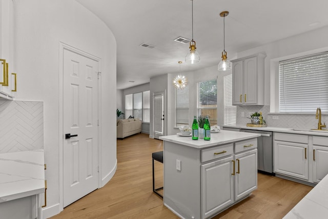 kitchen featuring light wood finished floors, hanging light fixtures, a kitchen island, a sink, and dishwasher