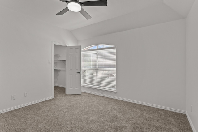 unfurnished bedroom with lofted ceiling, light carpet, a ceiling fan, baseboards, and a spacious closet