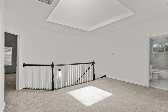 spare room featuring light carpet, visible vents, baseboards, and a raised ceiling