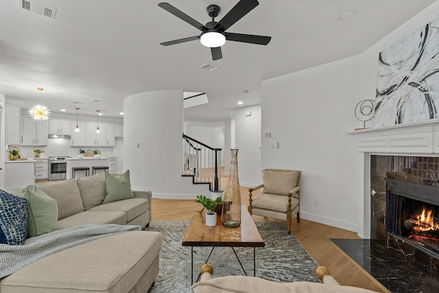 living room featuring a fireplace with flush hearth, visible vents, light wood-style floors, and stairway