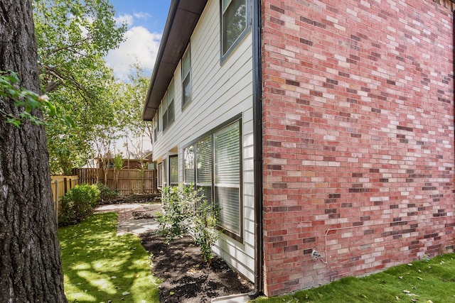 view of side of home with brick siding, a lawn, and fence