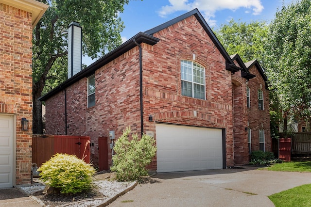 view of side of home featuring driveway, a garage, fence, and brick siding