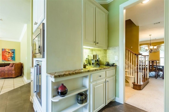 bar with crown molding, light stone countertops, stainless steel microwave, and an inviting chandelier