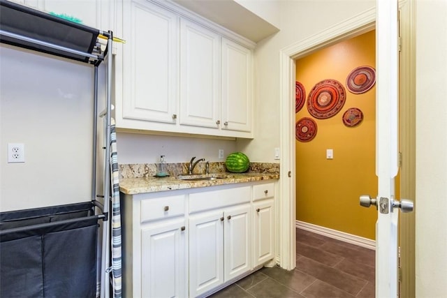 kitchen featuring white cabinetry, light stone countertops, sink, and dark tile patterned flooring