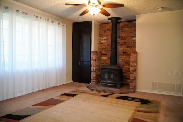 unfurnished living room with carpet flooring, a wood stove, ceiling fan, and a textured ceiling