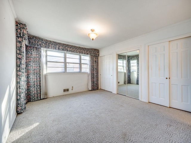 unfurnished bedroom with visible vents, multiple closets, and light colored carpet