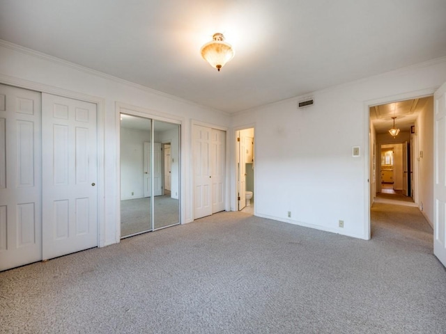 unfurnished bedroom with attic access, light colored carpet, ornamental molding, and two closets