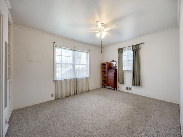 carpeted spare room featuring a ceiling fan, visible vents, and crown molding