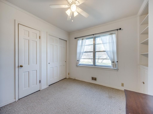 unfurnished bedroom with crown molding, two closets, light colored carpet, visible vents, and a ceiling fan