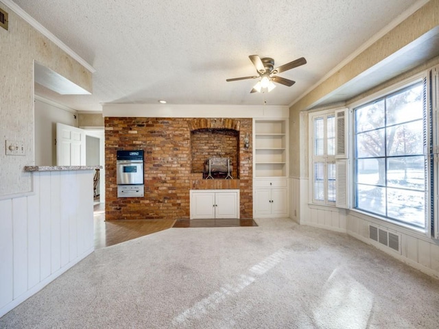 unfurnished living room with a textured ceiling, built in shelves, light carpet, visible vents, and ornamental molding