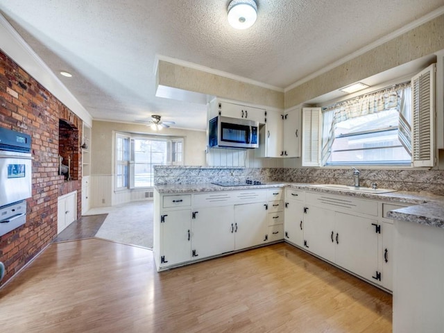 kitchen with a textured ceiling, oven, a sink, white cabinetry, and stainless steel microwave