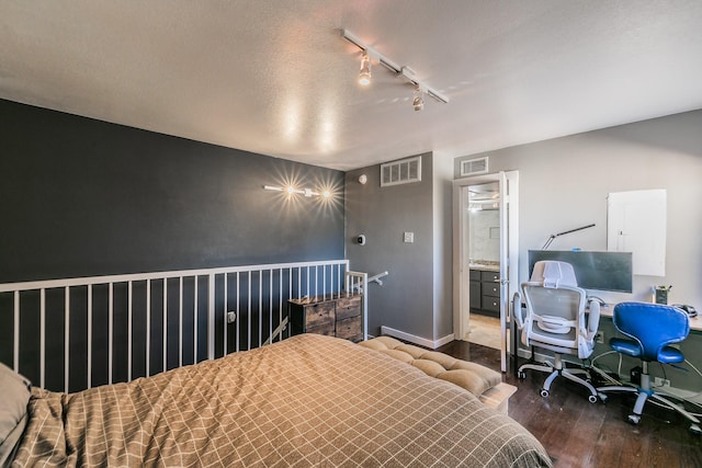 bedroom with a textured ceiling, track lighting, hardwood / wood-style flooring, and connected bathroom