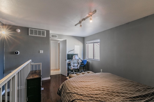 bedroom with dark hardwood / wood-style flooring, a textured ceiling, and track lighting