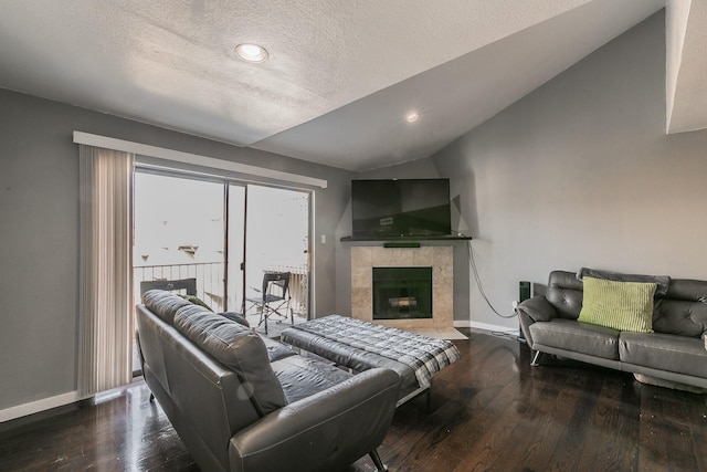 living room with a tiled fireplace, vaulted ceiling, hardwood / wood-style floors, and a textured ceiling