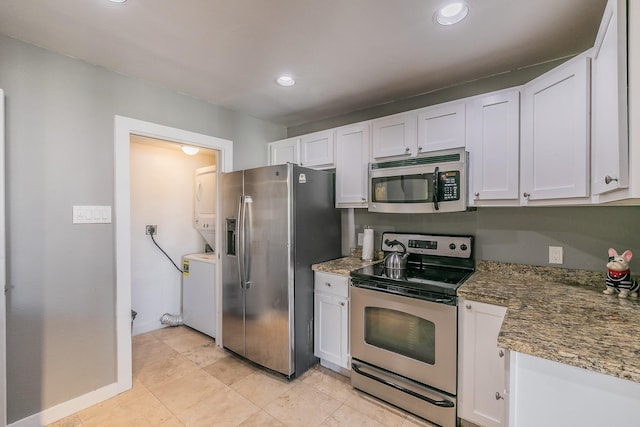 kitchen featuring dark stone counters, white cabinetry, stainless steel appliances, and stacked washer / drying machine