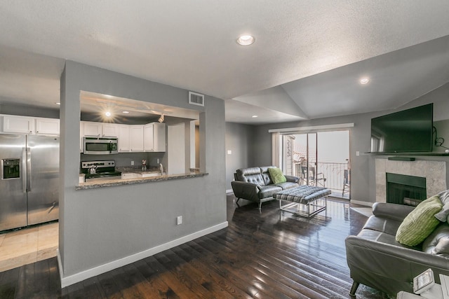 living room with lofted ceiling, dark wood-type flooring, sink, a textured ceiling, and a tiled fireplace