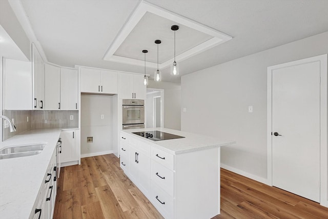 kitchen with black electric cooktop, a raised ceiling, sink, a kitchen island, and hanging light fixtures