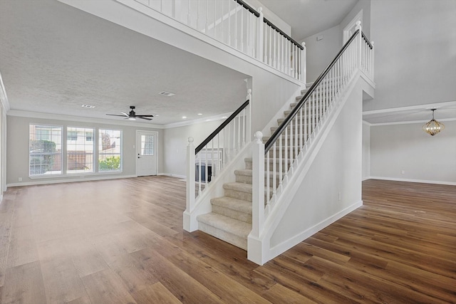 staircase featuring crown molding, a towering ceiling, ceiling fan with notable chandelier, and hardwood / wood-style flooring