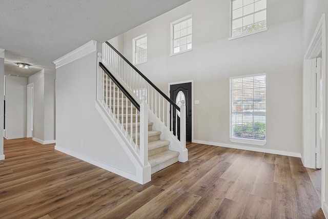 foyer featuring a towering ceiling, hardwood / wood-style floors, a textured ceiling, and crown molding